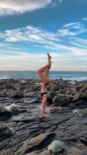 Beautiful girl in bikini practicing handstand on rocks by the sea short MP4 video