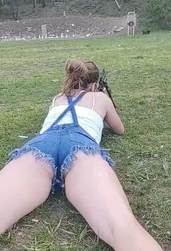 A_woman_wearing_denim_shorts_with_suspenders_is_shooting_in_a_prone_position